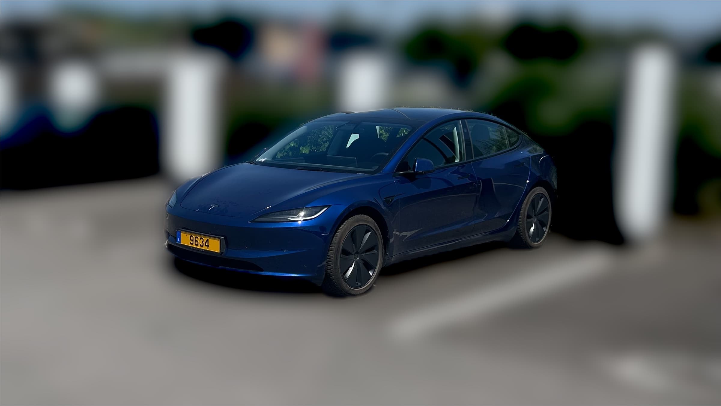 Tesla Model 3 plugged in at a Supercharger station on a sunny day